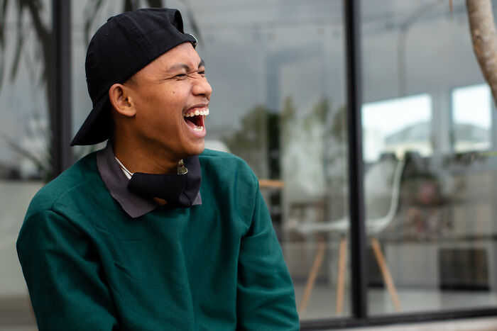 Young man wearing a backward cap laughing outdoors, showing signs you grew up sheltered with joyful expression and casual style
