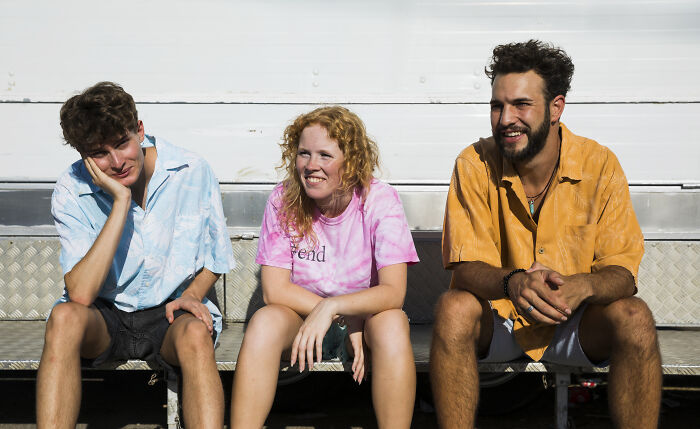 Three young adults sitting outdoors on metal steps, showing signs they grew up sheltered in casual summer clothing.
