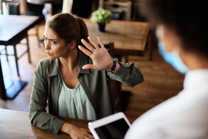 Young woman showing defensive gesture in a cafe, reflecting signs you grew up sheltered in social settings.