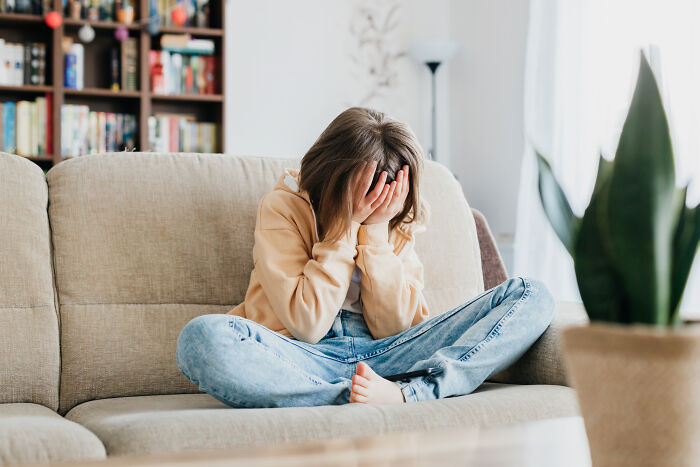 Teen sitting on a couch with head in hands, illustrating signs you grew up sheltered and feeling overwhelmed at home.