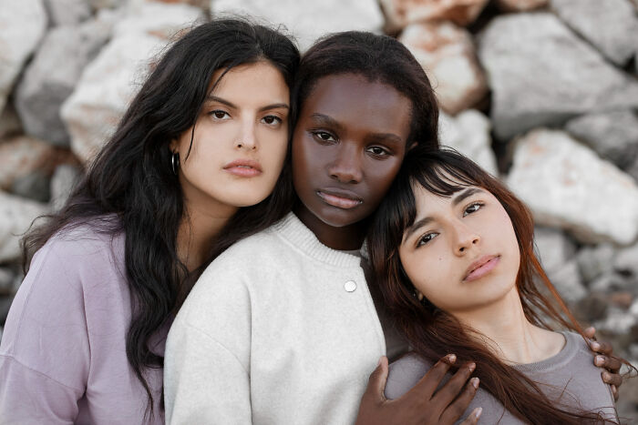 Three diverse young women close together outdoors, showing signs of having grew up sheltered in a natural setting.
