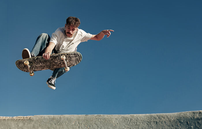 Young man performing a high skateboarding trick outdoors, illustrating signs you grew up sheltered in an urban setting.
