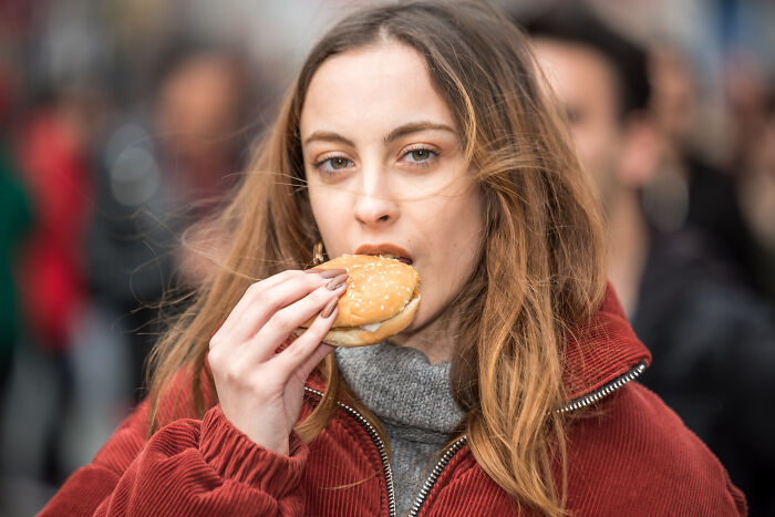 Young woman biting a burger outdoors, illustrating signs you grew up sheltered in a casual urban environment.