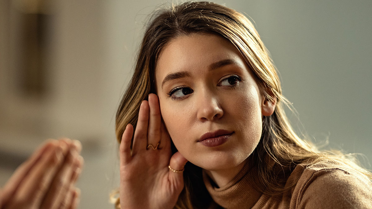 Young woman listening carefully with hand near ear, illustrating signs you grew up sheltered in a thoughtful setting