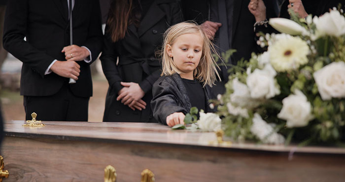 Young girl placing a flower on casket at a funeral, symbolizing family struggles with late wife and children’s memories. Young girl placing a flower on casket at a funeral, symbolizing family struggles with late wife and children’s memories.