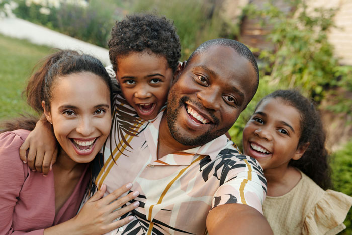 Happy family smiling outdoors with man running after kids and woman lounging on the couch in casual setting Happy family smiling outdoors with man running after kids and woman lounging on the couch in casual setting