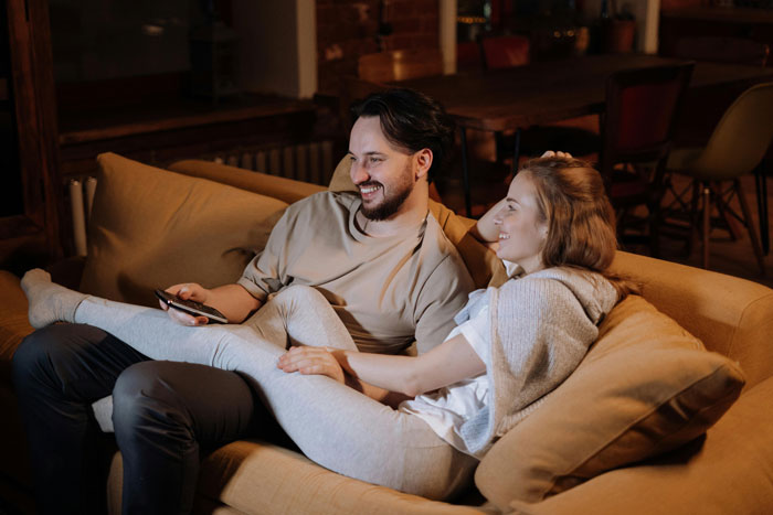 SIL lounges comfortably on the couch smiling while BIL looks ready to manage her kid in a cozy home setting. SIL lounges comfortably on the couch smiling while BIL looks ready to manage her kid in a cozy home setting.