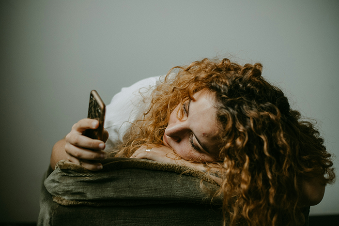 Young woman with curly hair resting on a couch, looking at her phone, reflecting on generational trauma conversation.