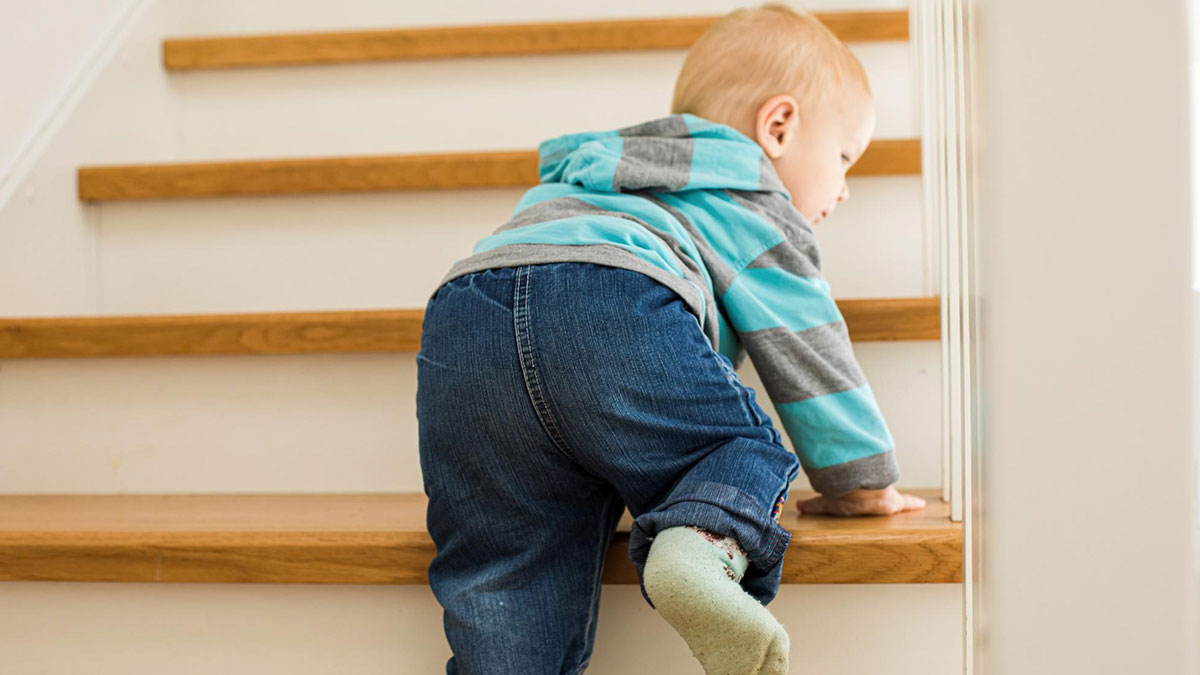 Toddler climbing wooden stairs in an indoor loft setting, highlighting concerns about unsafe loft environments and CPS visits.