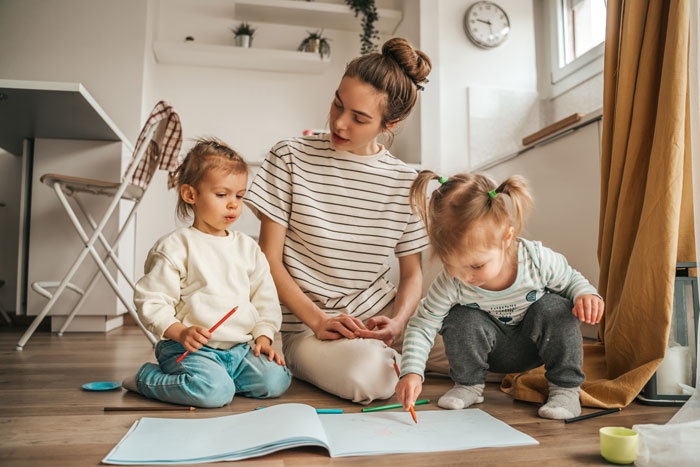 Young woman babysitting two toddlers drawing on paper indoors, illustrating babysitting challenges with unexpected kids. Young woman babysitting two toddlers drawing on paper indoors, illustrating babysitting challenges with unexpected kids.