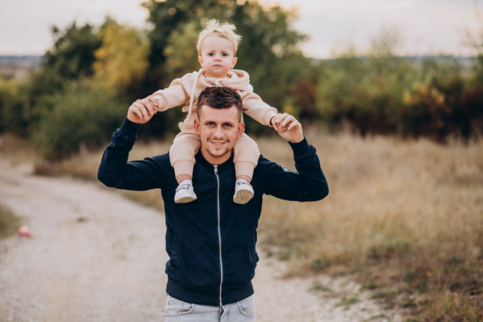 Man carrying toddler on shoulders outdoors, illustrating woman quitting babysitting after unexpected kids arrive from BIL. Man carrying toddler on shoulders outdoors, illustrating woman quitting babysitting after unexpected kids arrive from BIL.
