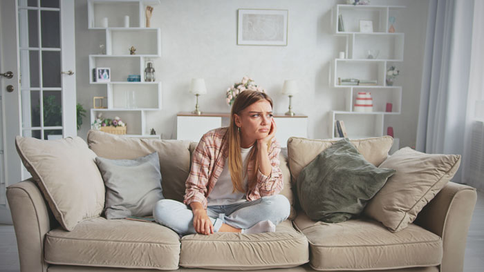 Young woman sitting on couch looking stressed and frustrated after unexpected babysitting with unfamiliar kids arrives. Young woman sitting on couch looking stressed and frustrated after unexpected babysitting with unfamiliar kids arrives.