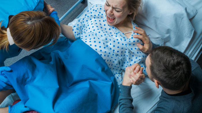 Woman in hospital gown giving birth with medical staff assisting and partner holding her hand during delivery scene Woman in hospital gown giving birth with medical staff assisting and partner holding her hand during delivery scene