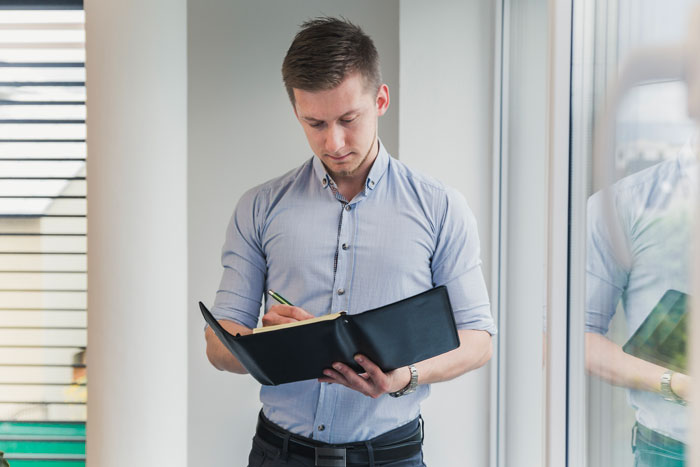 Man in a light blue shirt writing in a notebook near a window, symbolizing lady getting revenge on sister’s bad ex. Man in a light blue shirt writing in a notebook near a window, symbolizing lady getting revenge on sister’s bad ex.