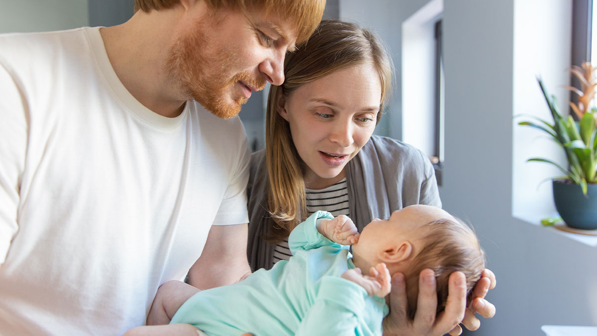 Young couple admiring their newborn baby in a bright room, highlighting baby naming and family dynamics.