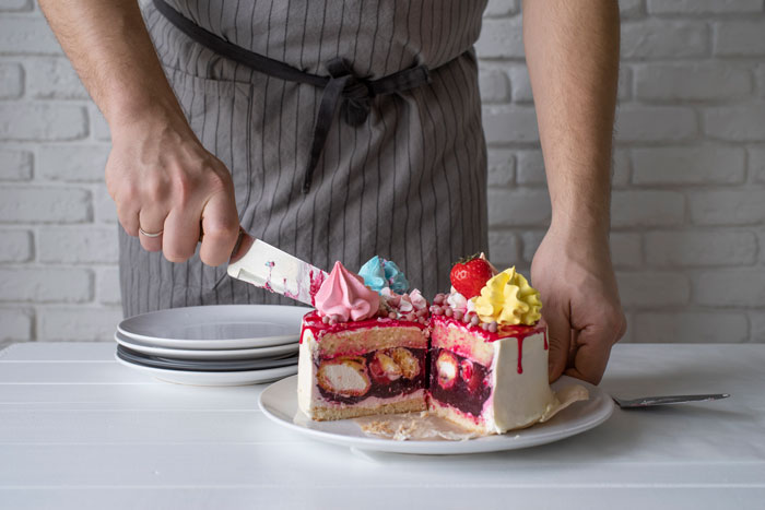 Person cutting a colorful custom baby shower cake with layers of cream and fruit on a white plate.