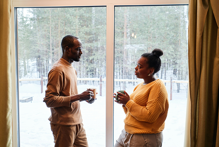 Couple having a serious conversation indoors near window, reflecting on secret ownership and rental of mom’s house. Couple having a serious conversation indoors near window, reflecting on secret ownership and rental of mom’s house.
