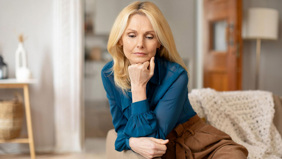Middle-aged woman in a blue blouse sitting pensively indoors, reflecting on issues related to stealing daughters trust fund.