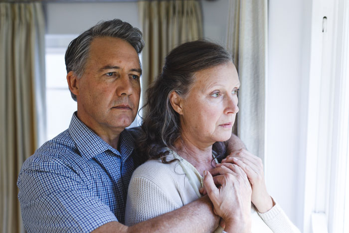 Middle-aged couple looking out a window, portraying concern and disturbed mental health in a tense moment. Middle-aged couple looking out a window, portraying concern and disturbed mental health in a tense moment.