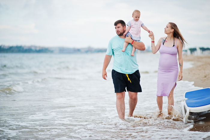 Family with baby walking on beach, illustrating woman’s disturbed mental health over stepdaughter’s baby identity. Family with baby walking on beach, illustrating woman’s disturbed mental health over stepdaughter’s baby identity.
