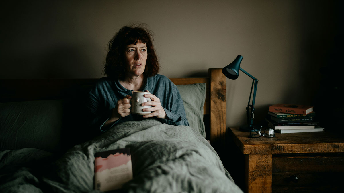 Woman in bed holding a mug, looking thoughtful and tired after being treated like a maid by hubby and teens.