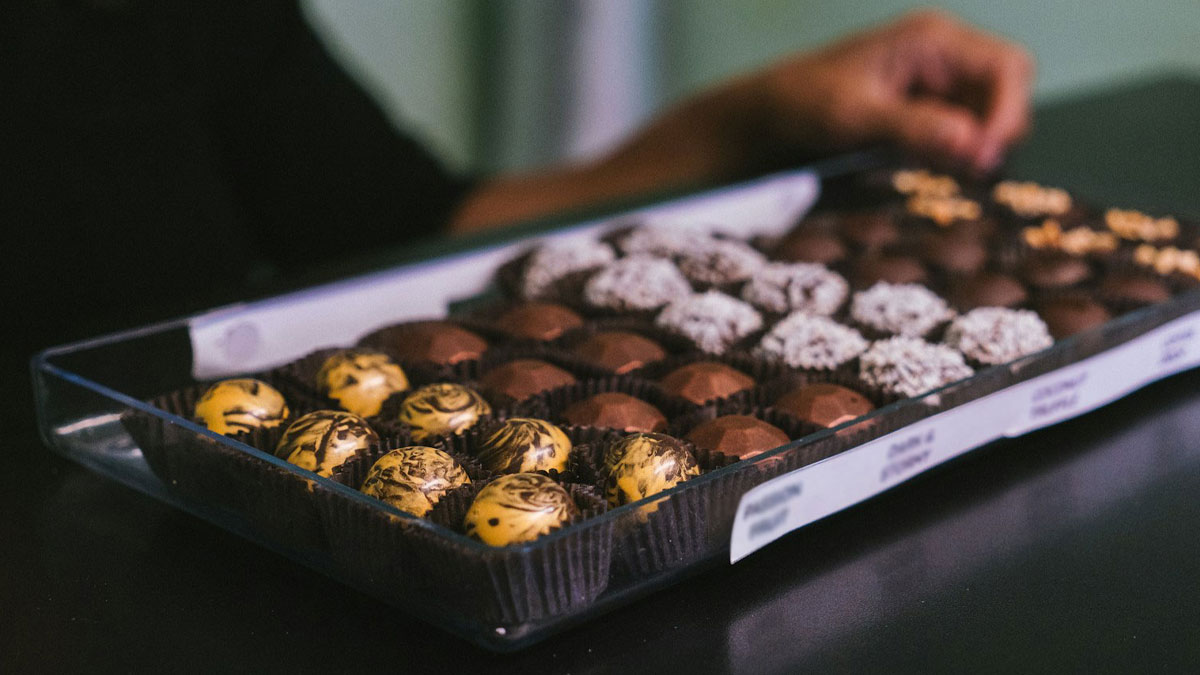 Assorted chocolates in a box being picked up by a person, illustrating creative revenge on bosses.
