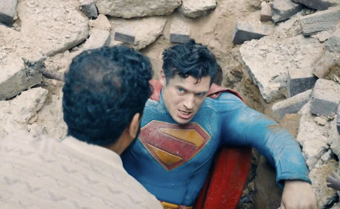 Superman in a blue suit with a red cape trapped in rubble, highlighting backlash against the woke Superman reboot.