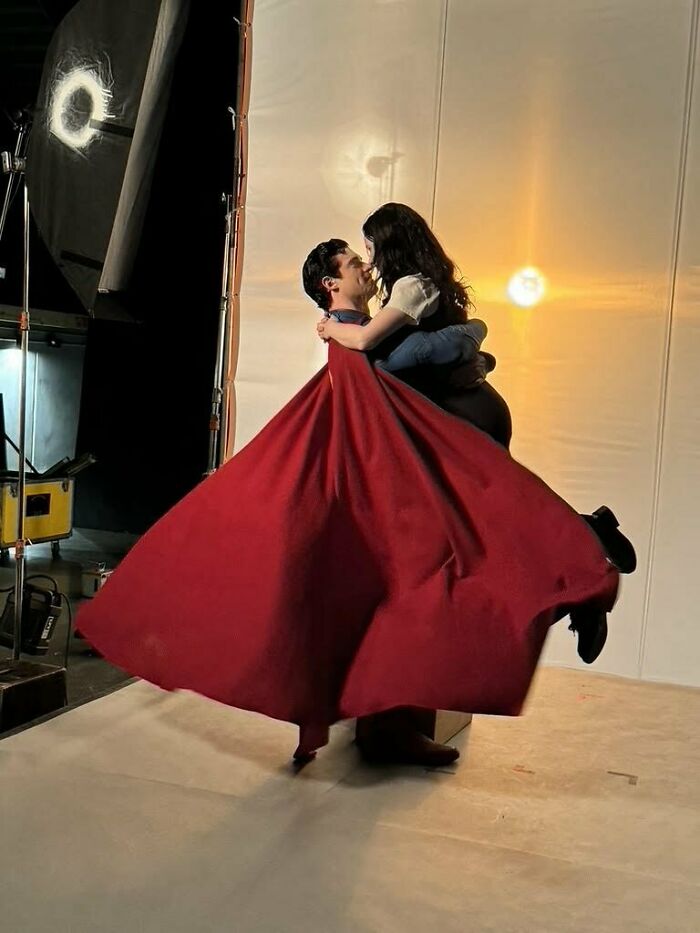 Superman reboot photoshoot with actor in red cape holding a woman, showcasing the film’s new look for woke Superman.