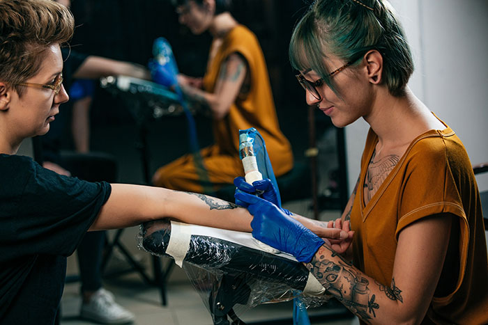 Tattoo artist wearing gloves carefully working on a client’s forearm in a studio focused on moral grounds. Tattoo artist wearing gloves carefully working on a client’s forearm in a studio focused on moral grounds.