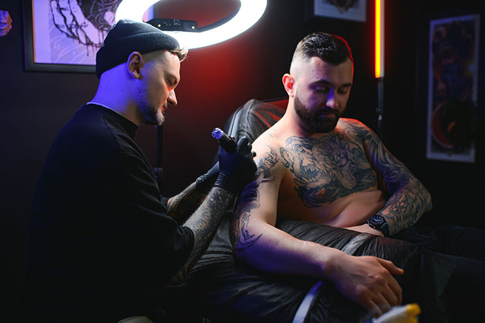 Tattoo artist working on a client’s arm in a dark studio, highlighting tattoo artists and jobs they decline on moral grounds. Tattoo artist working on a client’s arm in a dark studio, highlighting tattoo artists and jobs they decline on moral grounds.