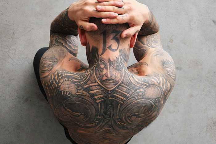 Tattoo artist with intricate back and neck tattoos showcasing designs they may decline based on moral grounds. Tattoo artist with intricate back and neck tattoos showcasing designs they may decline based on moral grounds.