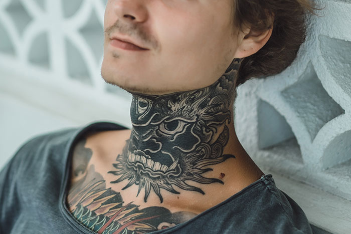Young man with intricate dragon neck tattoo and chest ink, showcasing bold tattoo art by skilled tattoo artists. Young man with intricate dragon neck tattoo and chest ink, showcasing bold tattoo art by skilled tattoo artists.