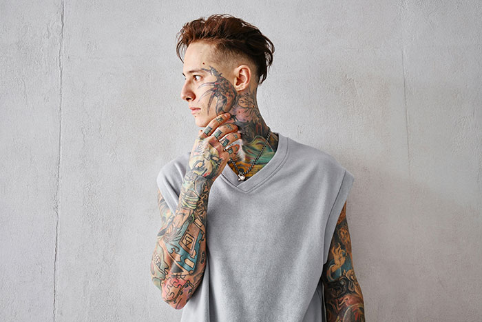 Tattoo artist with full sleeve and neck tattoos wearing gray sleeveless shirt, symbolizing jobs declined on moral grounds. Tattoo artist with full sleeve and neck tattoos wearing gray sleeveless shirt, symbolizing jobs declined on moral grounds.