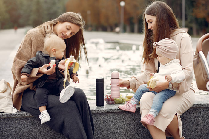 Teen babysitter holding child while sitting outdoors with another woman and toddler, highlighting babysitting challenges and respect issues.