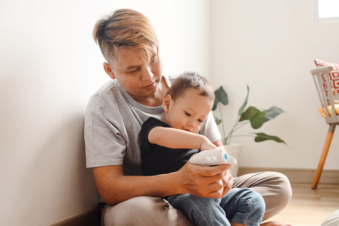 17-year-old babysitting sister’s kids, showing care and attention while sitting on the floor playing with a toy.
