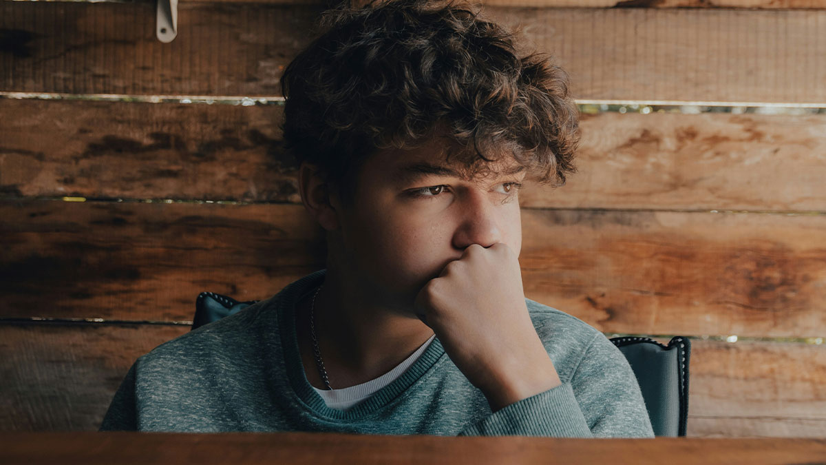 Teen boy looking thoughtful and shocked indoors, reflecting on estranged mom reaching out after 14 years separation.