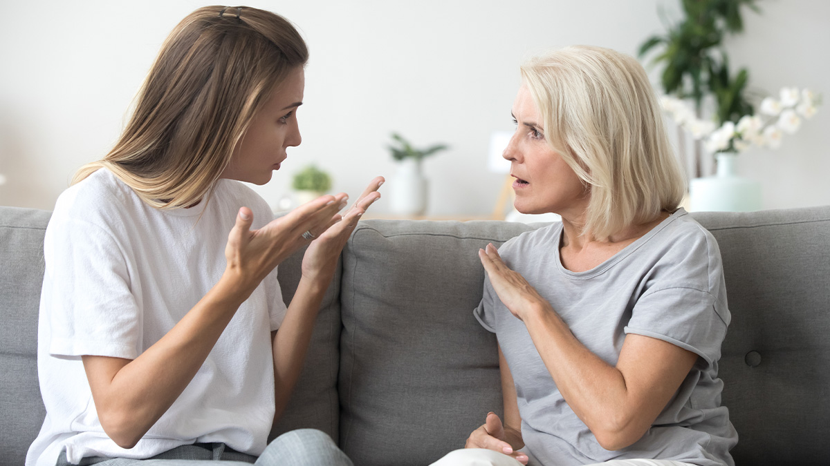 Middle-aged woman and younger woman having a heated argument on a couch over cheating and family issues.