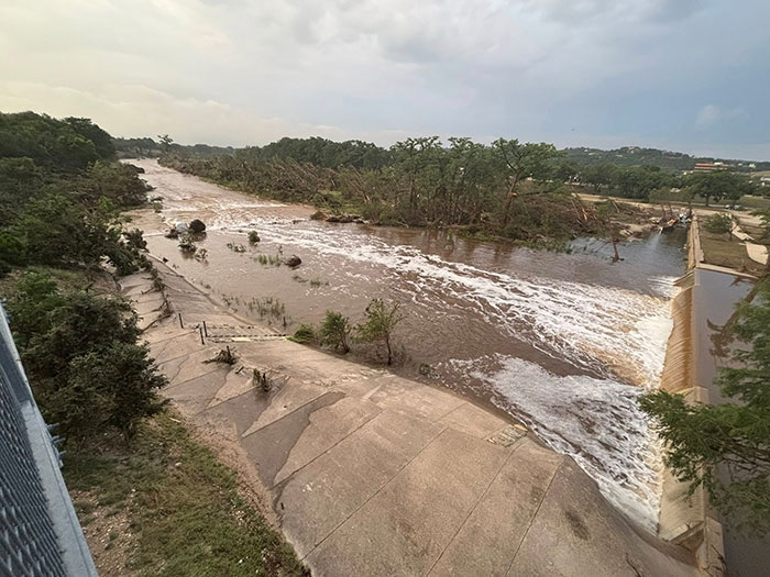 Flooded river in Texas with strong water flow and surrounding trees during a severe weather event causing disaster. Flooded river in Texas with strong water flow and surrounding trees during a severe weather event causing disaster.