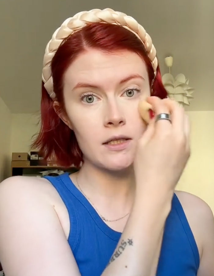 Professional escort applying makeup indoors, discussing racial discrimination and sparking debate in the industry.