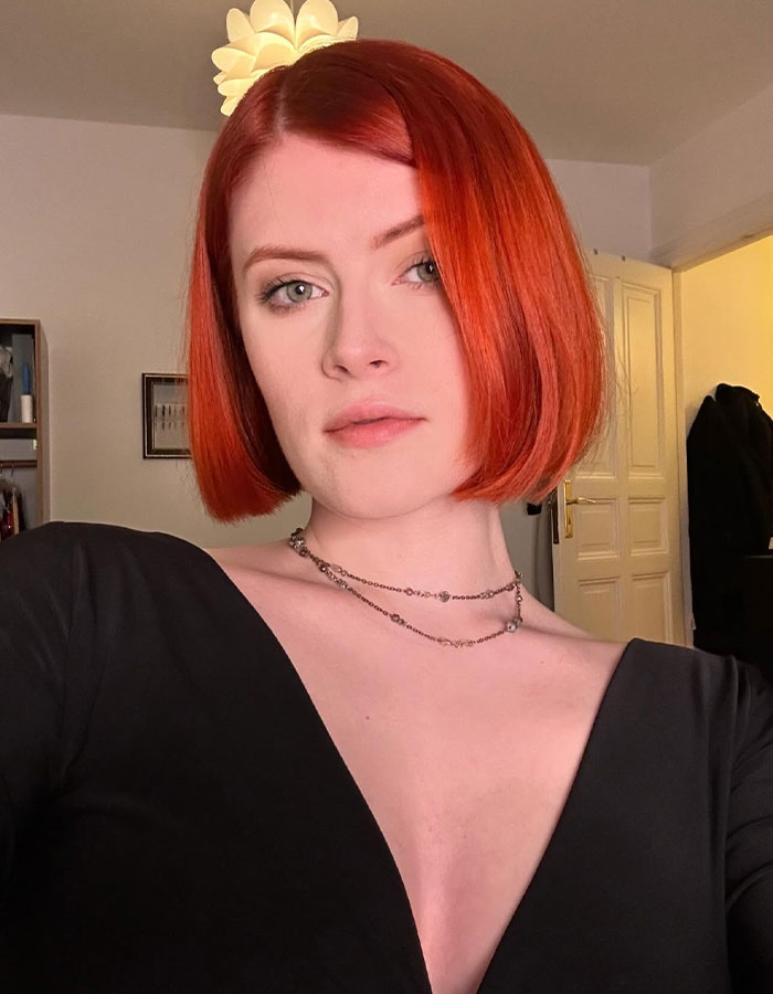 Young woman with red hair wearing a black top, representing a professional escort discussing racial discrimination in the industry.