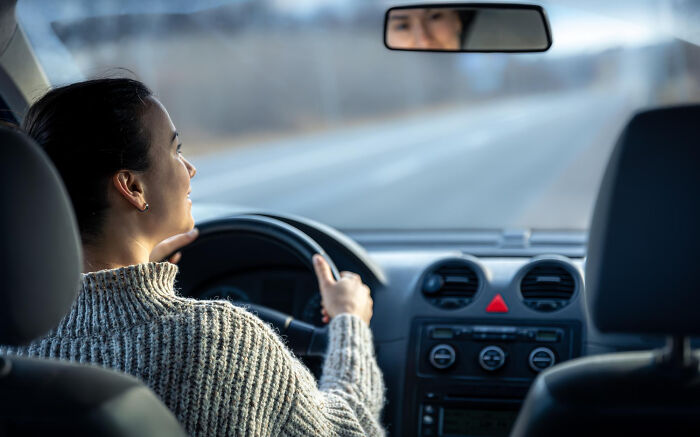 Woman driving a car peacefully on an empty road, reflecting trust and patience from the good old days disappearing.