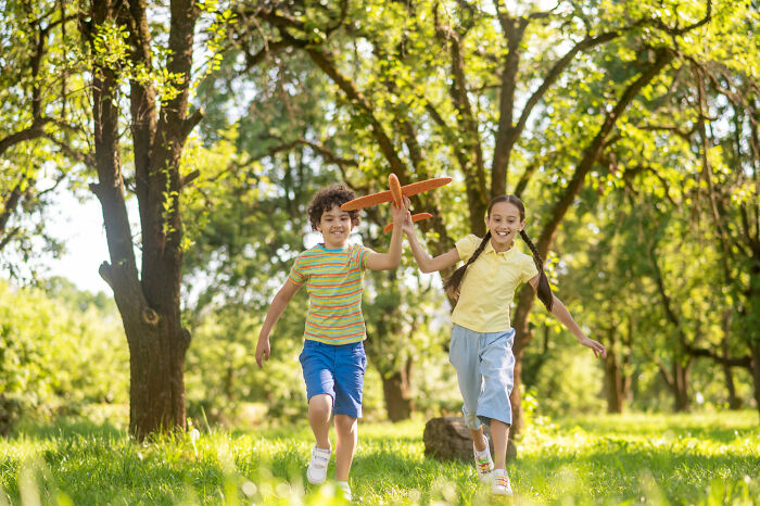 Two children playing with a wooden toy airplane outdoors, enjoying simple moments from the good old days.