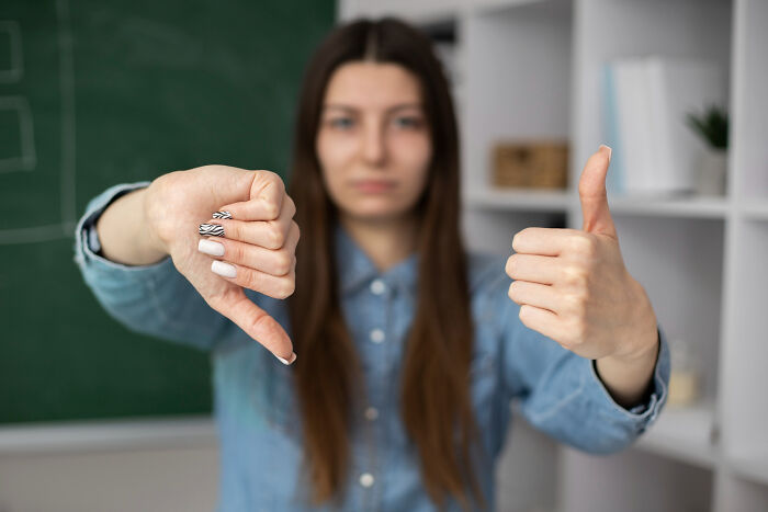 Young woman showing thumbs up and thumbs down, symbolizing trust and patience slowly disappearing from the good old days.