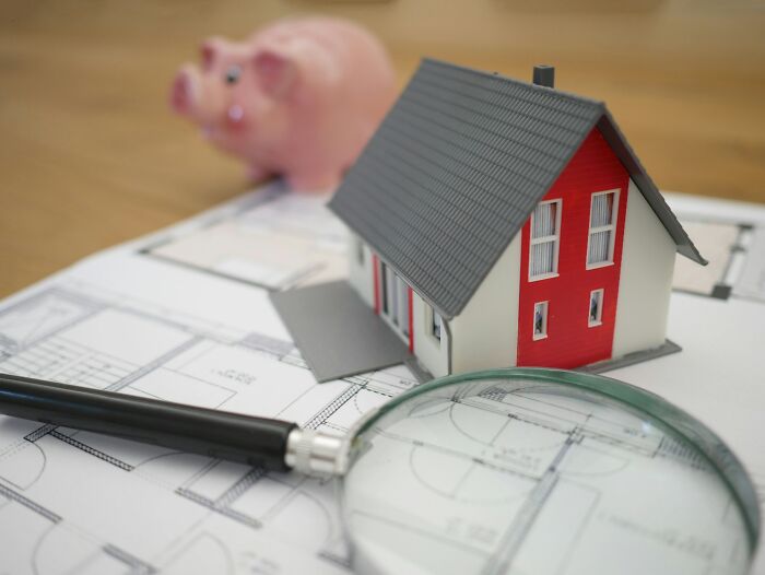 Model house and piggy bank on architectural plans with magnifying glass symbolizing people share reasons not divorced.