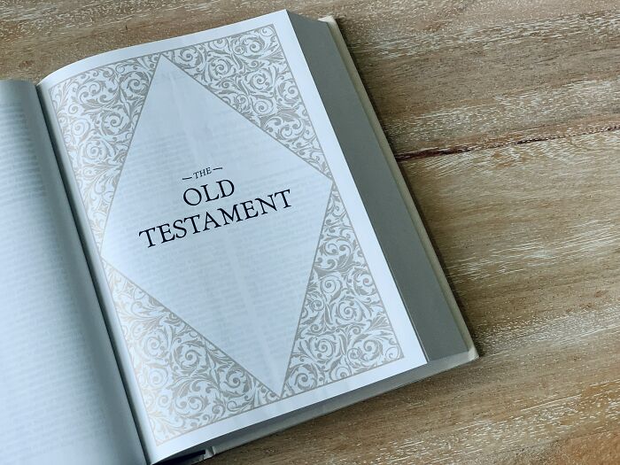 Open Bible showing the Old Testament title page on a wooden table, related to Jesus wrote the Bible myth.
