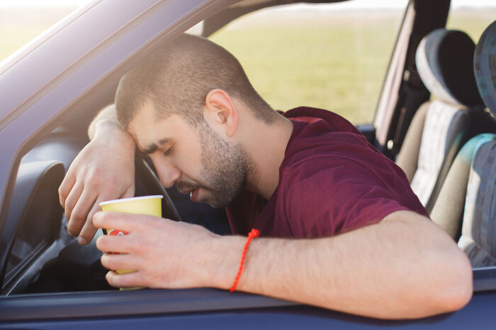 McDonald’s employee exhausted and resting head on car door holding a cup after a long shift sharing bizarre experiences.