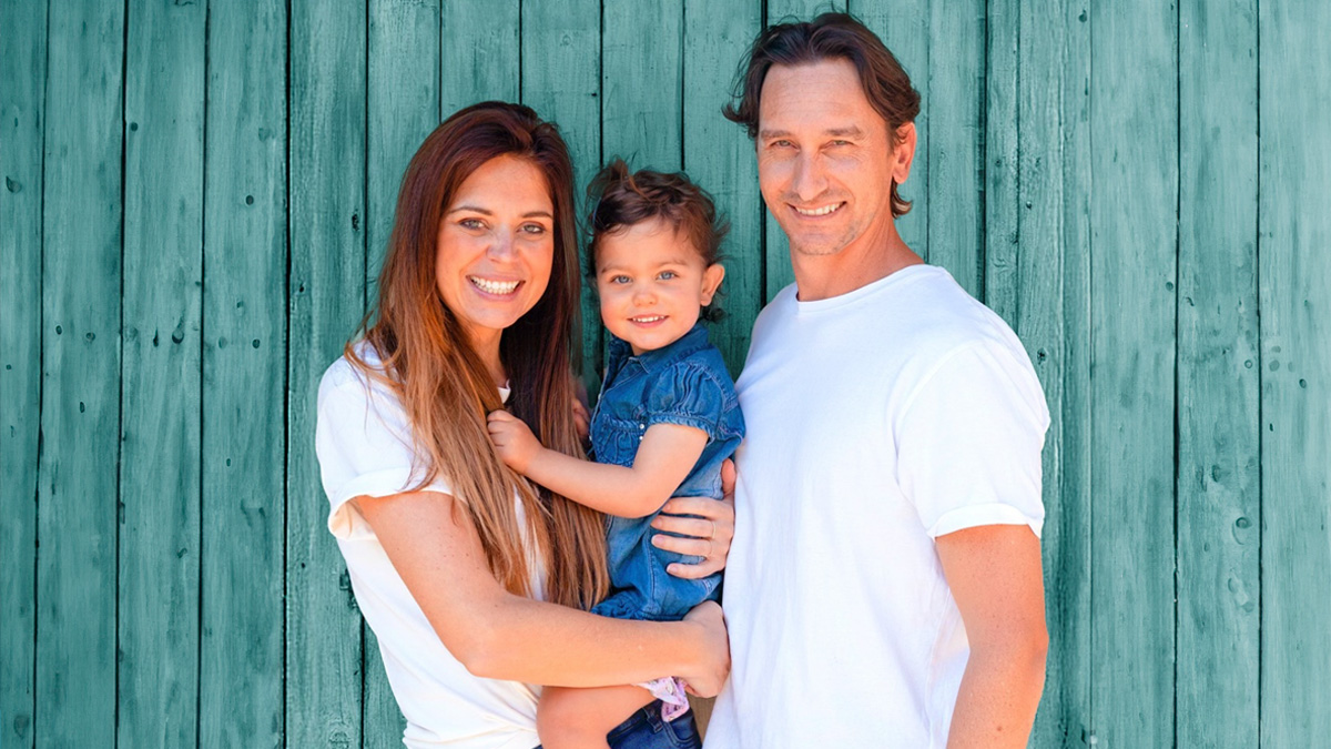Happy family with toddler posing in front of a teal wooden wall, highlighting toddler traveled to 13 countries experiences.