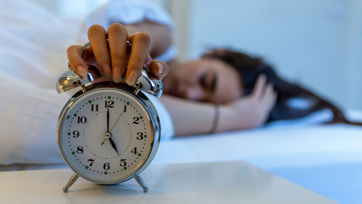 Tourist pressing alarm clock snooze while oversleeping in bed, showing frustration about not being woken up by guide.