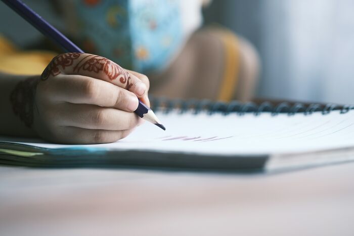 Close-up of a hand holding a pencil and writing in a notebook illustrating bizarre beliefs people still fall for.