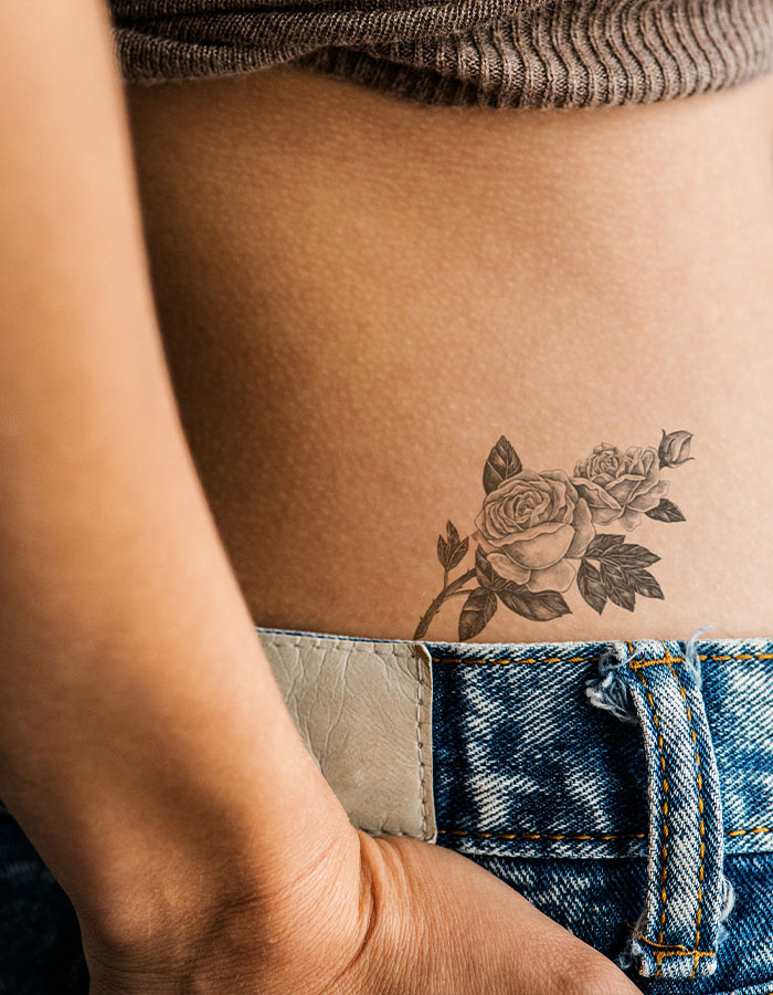 Close-up of a floral tramp stamp tattoo on a lower back near denim jeans and a cropped sweater. Close-up of a floral tramp stamp tattoo on a lower back near denim jeans and a cropped sweater.